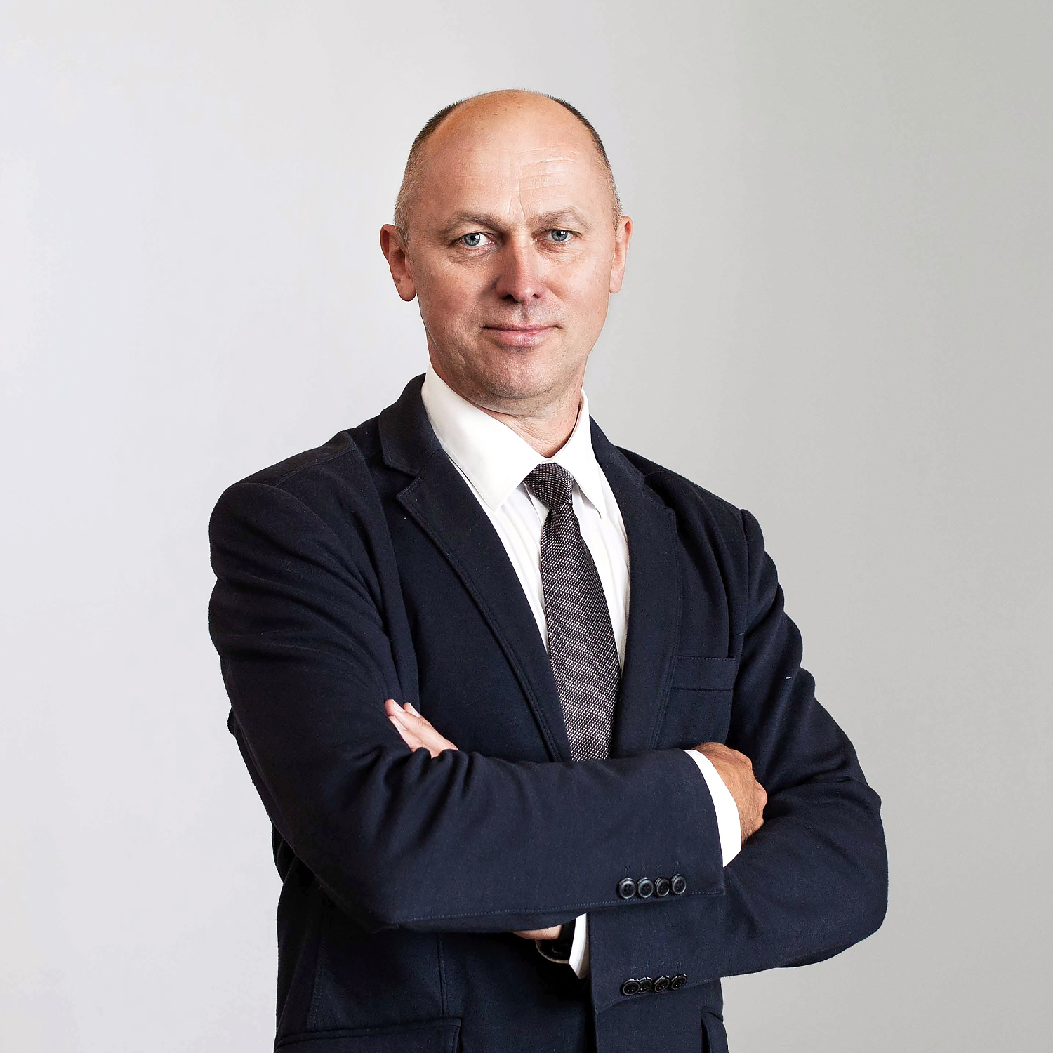 Portrait photo &ndash; a middle-aged man with short blond hair, wearing a dark suit and white shirt, his arms folded. He is looking directly at the camera with a neutral gaze. The photo introduces Prof. Dr. Valdas Eidukynas, team member of KTU numerical simulation competence centre.